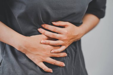 Karın ağrısı, kramp ya da sindirim güçlüğü belirtileri gösteren karnını iki eliyle tutan bir kadının yakın çekimi..