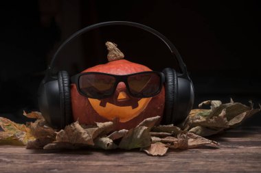 Güneş gözlüğü ve kulaklıklarla aydınlatılmış Cadılar Bayramı balkabağı.