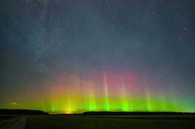 Yeşil ve kırmızı ışınlı parlak aurora borealis kırsal bir arazide yıldızlı bir gece gökyüzünün altında