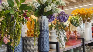 Assortment of fresh flowers in various decorative vases, displayed on a shelf, highlighting vibrant colors and textures in a bright floral shop atmosphere