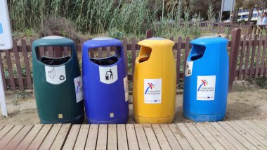 Canlı renklerde dört farklı çöp tenekesi ahşap bir yol boyunca yerleştirilerek, doğal bir ortamda geri dönüşüm ve uygun atık imhası teşvik edilir.