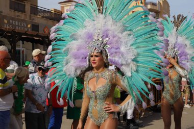 Orihuela Costa, İspanya - 17 Mart 2024: Aziz Patrick Günü geçidi. Parlak bir karnaval kostümü ve büyük tüylü başlık giyen kadın, festival atmosferinde izleyicilerle çevrili bir tören sırasında poz veriyor.