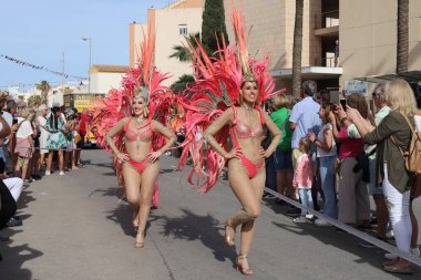 Orihuela Costa, İspanya - 17 Mart 2024: Aziz Patrick Günü geçidi. Canlı bir festival sırasında renkli kostümlü iki kadın dansçı, coşkulu bir kalabalık ve şenlikli dekorasyonlarla çevrili bir caddede geçit töreni yapıyor.
