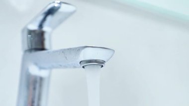 Gündüz vakti modern bir mutfak musluğundan su akar. Parlak bir ortamda.