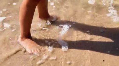 Sahilde çıplak ayakla yürürken öğleden sonra güneş bacakları etrafında süzülürken