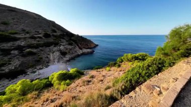 Güneşli bir günde açık gökyüzü ve uzak tepelerle deniz kıyısında gezinmek.