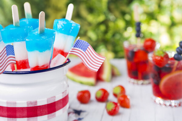 Red-white-and-blue popsicles on an outdoor table with summer drinks