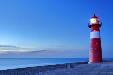 Kırmızı ve beyaz deniz feneri ve alacakaranlıkta açık bir gökyüzü