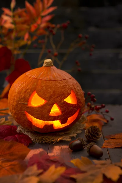 Queimando Jack O 'Lantern em uma mesa rústica com decorações de outono — Fotografia de Stock
