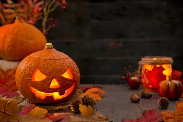 Queimando Jack O 'Lantern em uma mesa rústica com decorações de outono — Fotografia de Stock