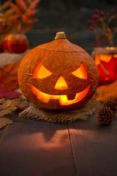 Queimando Jack O 'Lantern em uma mesa rústica com decorações de outono — Fotografia de Stock