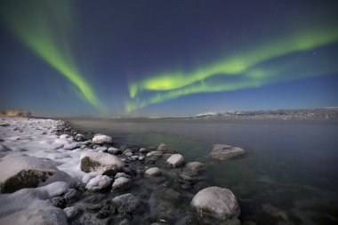 Aurora borealis Kuzey Norveç'te ay ışığının aydınlattığı bir fiyort üzerinde