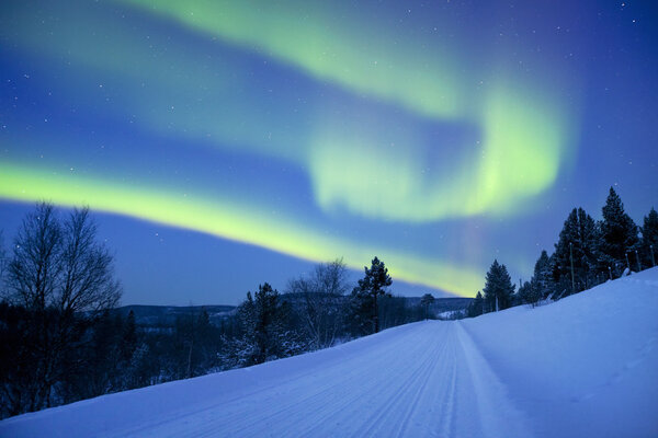 Aurora borealis over a road through winter landscape, Finnish La