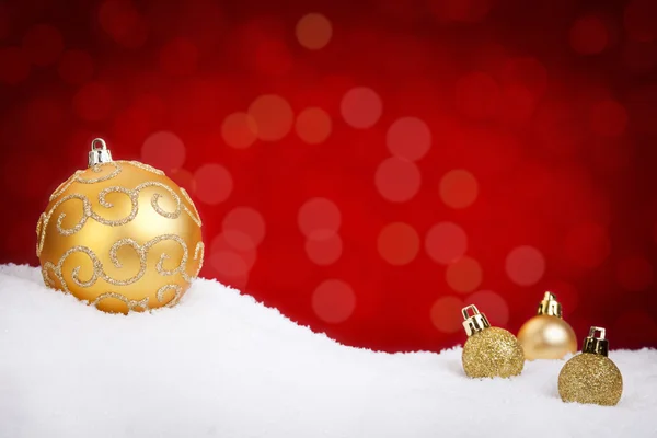 Baldes de Natal de ouro na neve com um fundo vermelho — Fotografia de Stock