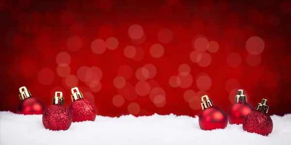 Rode kerstballen op sneeuw met een rode achtergrond — Stockfoto