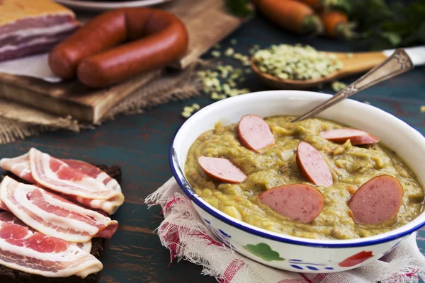 Traditionele Nederlandse erwtensoep en ingrediënten op een rustieke tabel — Stockfoto