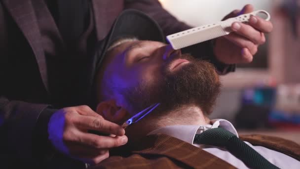 Barber cutting beard of caucasian male with the use of scissors. — Stock Video