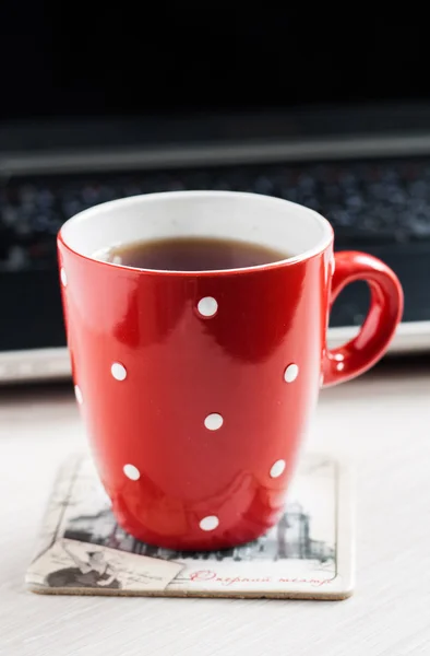 Czerwony kubek w grochu na tle ekranu laptopa — Zdjęcie stockowe