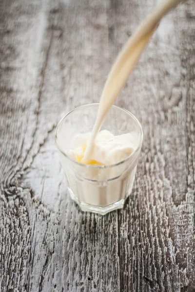 Le lait est versé dans un verre sur un fond en bois — Photo