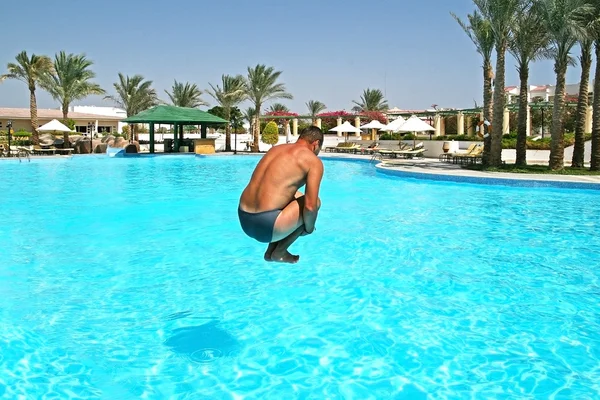 Homme saute dans la piscine dans une station tropicale — Photo