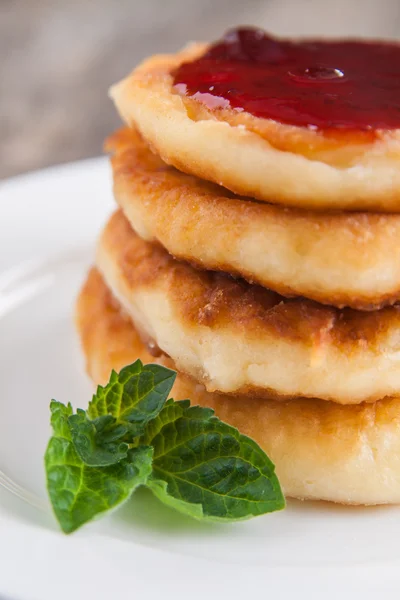 Stack of cheesecakes with jam on a white plate on a dark wooden — Stock Photo, Image