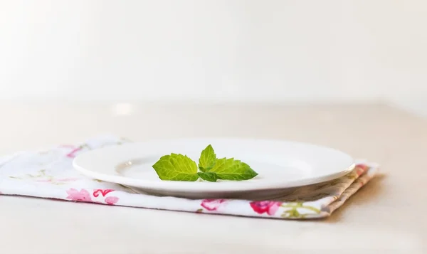 Hojas de menta en un plato blanco sobre un fondo blanco — Foto de Stock