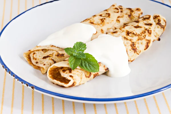 Crepes finos panqueques enrollados con crema agria menta en un plato —  Fotos de Stock