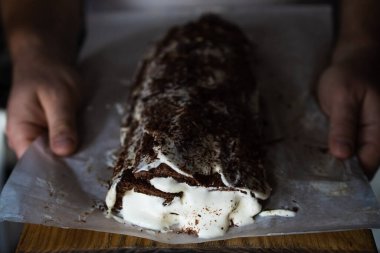 Geleneksel bir Noel çikolata rulosu kremalı, arka plandaki Noel ağacı ışıklarına karşı siyah arka planda, bir adam tarafından tutulur.