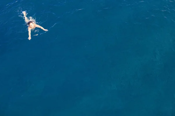 Воздушный вид сверху счастливая молодая женщина в черном купальнике плавает в Красном море, Египет, Шарм-эль-Шейх. Отдых и приключения. Голубая вода. Вид сверху на ленивую девушку, отдыхающую в море-океане. Копирование пространства — стоковое фото