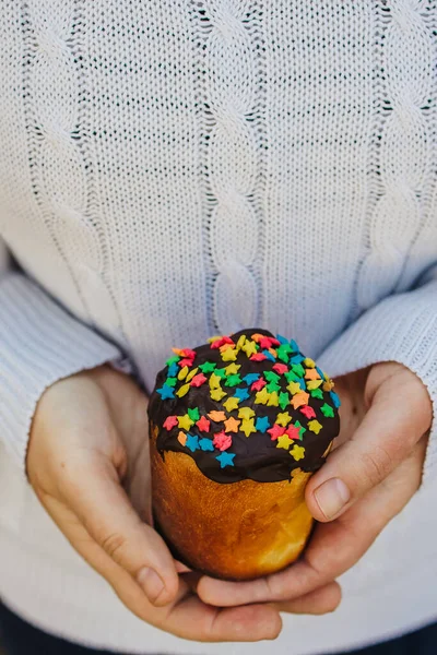 Cropped female hands on the background of a white knitted sweater holding a traditional Easter cake — Stock Photo, Image