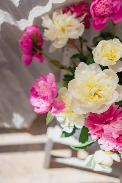 Um buquê de peônias brancas e rosa frescas em um vaso de vidro transparente com belas sombras perto de um tule de cortina branca, em borrão — Fotografia de Stock