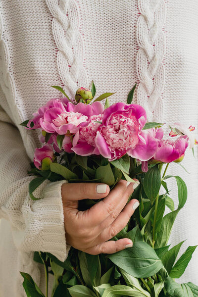 cropped young woman in white knitted sweater holding a bouquet of fresh flowers pink peonies