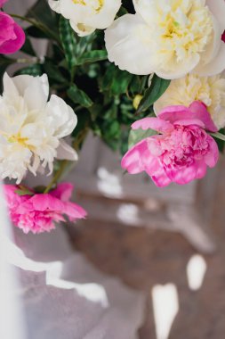 şeffaf bir vazoda beyaz ve pembe şakayıklardan oluşan bir buket. Beyaz perde tülünün yanında, bulanık bir vazoda güzel gölgeler var.