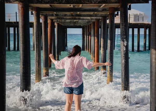 Turkey, Mediterranean Sea. Young woman turned away from the camera, running away from the waves under a wooden pier — Stock Photo, Image