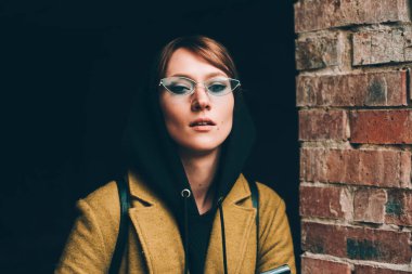 Zeytin rengi uzun paltolu, kapüşonlu kazaklı güzel bir kız. Siyah arka planda kapüşonlu kadın portresi