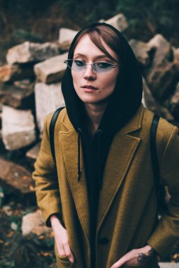 Zeytin rengi uzun paltolu, kapüşonlu kazaklı güzel bir kız. Siyah arka planda kapüşonlu kadın portresi