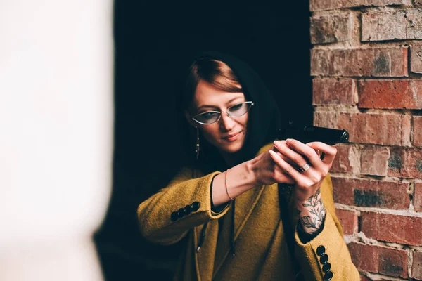 Pretty young girl in olive long coat, hooded sweatshirt. Portrait of woman with hood on dark background — Stock Photo, Image