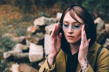 Zeytin rengi uzun paltolu, kapüşonlu kazaklı güzel bir kız. Siyah arka planda kapüşonlu kadın portresi