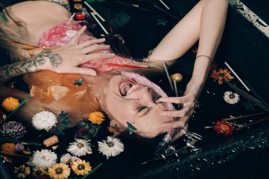 Çöplerle, çevreyle ya da polution konseptiyle dolu siyah banyoda korkmuş çıplak bir kız..