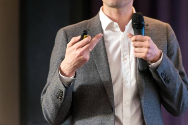 İş ve konuşma konusu: Gri takım elbiseli adam elinde siyah bir mikrofon ve multimedya projektörü tutuyor.