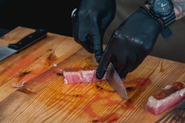 Lokantada siyah eldiven giyen şef tahtadan ton balıklı biftek yapıyor.