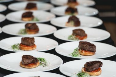 Siyah eldivenli bir şef restoranda masada hamburger servis ediyor. Siyah masa örtüsü