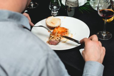 İyi bir restoranda yemek yiyen bir adam fast food 'u çatal ve bıçakla yer, yakın plan.