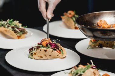 Restorandaki şef lahana salatası ve salsa soslu baharatlı karidesli taco yapıyor. Şef takolara karides koyar.