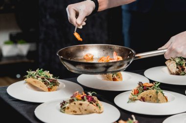 Restorandaki şef lahana salatası ve salsa soslu baharatlı karidesli taco yapıyor. Şef takolara karides koyar.