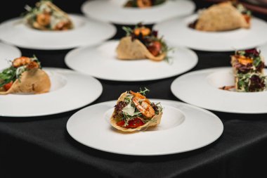 Salsa ve lahana salatalı baharatlı karidesli taco yemeye hazır bir masa. Masadaki beyaz tabakta birkaç taco var.