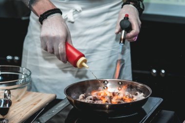 Şef, Brezilya yemeği yapmak için restoranda metal bir tavada küçük ahtapot pişirir. Pan yanıyor..