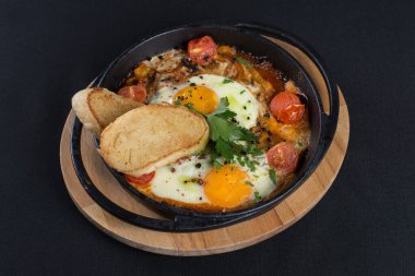 Sağlıklı kahvaltı shakshuka - kızarmış yumurta, soğan, dolmalık biber, domates ve baharatlar eski ahşap kalas üzerinde dökme demir güveç, dövüş açısı. Siyah masa örtüsü