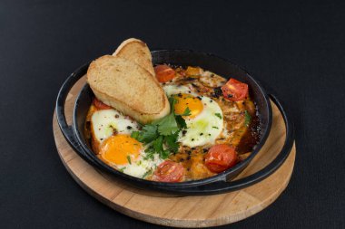 Sağlıklı kahvaltı shakshuka - kızarmış yumurta, soğan, dolmalık biber, domates ve baharatlar eski ahşap kalas üzerinde dökme demir güveç, dövüş açısı. Siyah masa örtüsü