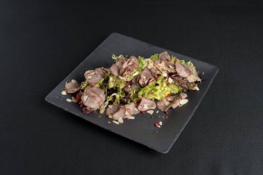 Tütsülenmiş ördek etli salata, siyah seramik tabakta badem taneli tatlı ve ekşi sos.